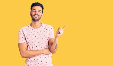 Genç, yakışıklı, günlük kıyafetler giyen, gülümseyen, eli ve parmağı kenarda mutlu bir adam. 