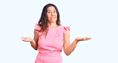 Genç, güzel, esmer, sıradan bir elbise giyen, kafası karışmış, kolları ve elleri havada bir kadın. şüphe kavramı. 