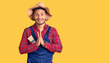 Yakışıklı Latin Amerikalı, giyimli, tamirci üniforması giyen, elleriyle dua eden, affedilmek isteyen, kendinden emin, gülümseyen genç adam.. 