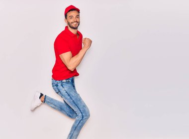 Mutlu gülümseyen üniformalı yakışıklı İspanyol teslimatçı. Yüzünde tebessümle zıplıyor, beyaz arka planda yumruklar havada kutluyor..