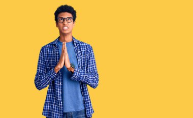 Sıradan kıyafetler ve gözlük takan genç Afro-Amerikalı adam elleri bağlı yalvarıyor ve dua ediyor. Yüzünde umut ifadesi var. Çok duygusal ve endişeli. Yalvarıyor. 