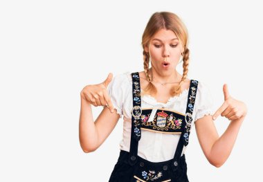 Oktoberfest elbisesi giymiş genç, sarışın bir kadın. İlan veren parmaklarıyla işaret ediyor. Şaşırmış bir yüz ve açık bir ağız. 