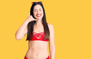 Bikini giyen, bikinili, güzel beyaz bir kadın telefonla el ve parmaklarıyla jest yapıyor, telefonda konuşuyor gibi. iletişim kavramları. 