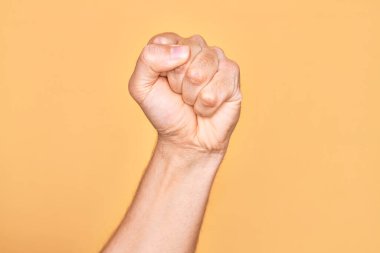 İzole edilmiş sarı arka planda, protesto ve devrim hareketleri yapan, güç ve güç gösterisi yapan beyaz bir gencin eli.