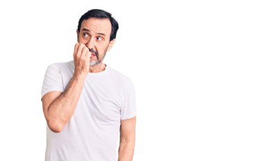 Orta yaşlı yakışıklı bir adam günlük tişört giyiyor stresli ve gergin görünüyor ve elleri ağız tırnağı yiyor. anksiyete. 