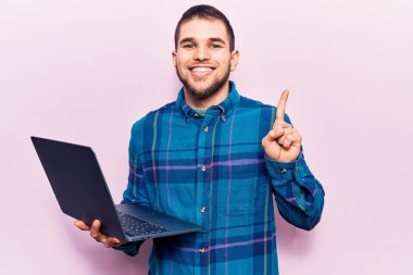 Genç yakışıklı adam dizüstü bilgisayar kullanarak çalışıyor. Bir fikir ya da soru sorarak gülümsüyor. Mutlu yüzle işaret ediyor. 