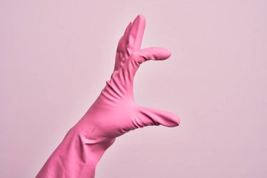 İzole edilmiş pembe arka plan üzerinde temizlik eldiveni olan beyaz bir adamın eli. Görünmez bir şeyi alıp, parmaklarında boşluk gösteren bir nesneyi tutuyor.