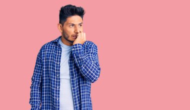 Yakışıklı Latin Amerikalı, rahat gömlekli, gergin ve ağzı tırnak yiyen elleri olan bir genç. anksiyete. 