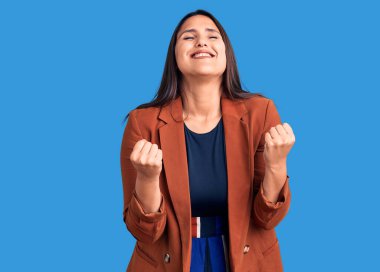 Zarif kıyafetler giyen güzel esmer bir kadın. Çok mutlu ve heyecanlı. Kolları havada, gülümseyen ve başarı için bağıran kazanan bir jest yapıyor. kutlama konsepti. 