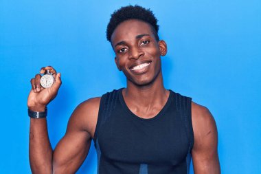 Elinde kronometre tutan Afro-Amerikalı genç adam pozitif ve mutlu görünüyor ve kendine güvenen bir gülümsemeyle dişlerini gösteriyor. 