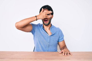 Yakışıklı İspanyol bir adam, gündelik giysiler içinde masada oturuyor, şok içinde yüzünü ve gözlerini kapıyor, utanmış bir ifadeyle parmaklarından bakıyor.. 