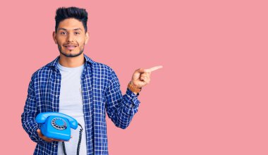 Yakışıklı Latin Amerikalı genç adam elinde klasik bir telefonla gülümsüyor mutlu bir şekilde elini ve parmağını yana doğru uzatıyordu. 