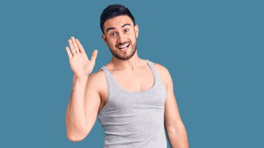 Mayolu ve kolsuz tişörtlü genç yakışıklı adam merhaba diyor mutlu ve güler yüzlü, dostça bir jest. 