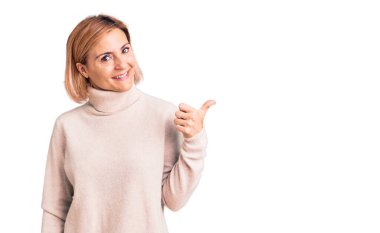 Sıradan kıyafetler giyen, gülen yüzlü genç sarışın kadın başparmağıyla yan tarafa bakıyor ve işaret ediyor.. 