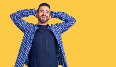 Genç İspanyol bir adam günlük kıyafetler giyiyor rahatlıyor ve esniyor, kolları ve elleri başının arkasında mutlu bir şekilde gülümsüyor. 