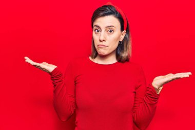 Gündelik giysiler giyen genç ve güzel bir kadın habersiz ve kolları açık, hiçbir fikrim yok ve şüpheli bir yüzüm var.. 