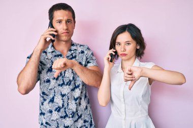 Akıllı telefonda konuşan güzel bir çift. Kızgın suratlı, negatif işaretli, baş parmakları aşağıda, reddedilme kavramlı. 