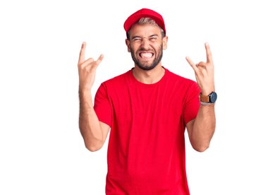 Tişört giyen ve şapkalı genç sarışın adam çılgın bir ifadeyle bağırıyor elleri havada rock sembolü yapıyor. Müzik yıldızı. ağır kavram. 