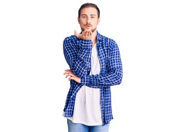 Genç, beyaz, sıradan kıyafetler giyen yakışıklı bir adam kameraya bakıyor ve havada bir öpücük savuruyor. Güzel ve seksi. aşk ifadesi. 