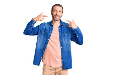 Gündelik kıyafetler giyen, neşeli gülümseyen, parmaklarıyla ve ağzıyla işaret eden genç yakışıklı bir adam. diş sağlığı kavramı. 