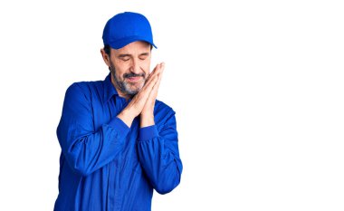 Orta yaşlı, yakışıklı, mekanik üniforma giyen, yorgun uyuyan, hayal kuran, elleriyle poz veren ve gözleri kapalı gülümseyen bir adam.. 