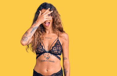 Dövmeli, iç çamaşırlı genç bir İspanyol kadın. Şoka girmiş, yüzünü ve gözlerini kapamış, utangaç ifadesiyle parmaklarından bakıyor.. 