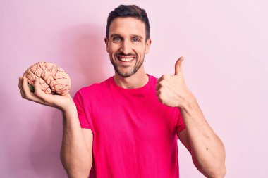 Genç yakışıklı adam beyni soyutlanmış pembe arka planda tutan mutlu ve pozitif gülümseyen, başparmağını kaldıran mükemmel ve onay işareti yapan bir bakım hafızası istiyor.