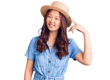 Yazlık şapkalı güzel Çinli kız gülümseyerek tek parmağıyla kafasını işaret ediyor, harika bir fikir ya da düşünce, iyi bir hafıza. 