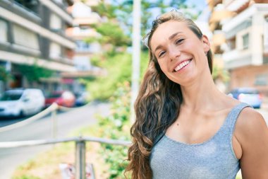 Genç sarışın kadın gülümsüyor. Şehrin caddesinde mutlu bir şekilde yürüyor.