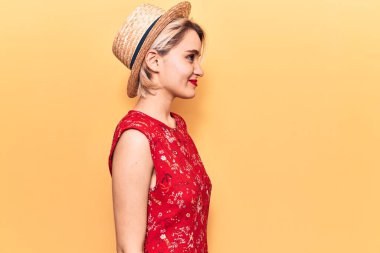 Yazlık şapka takan genç ve güzel sarışın kadın, rahat bir görünüm ve kendine güvenen bir gülümsemeyle poz veriyor.. 