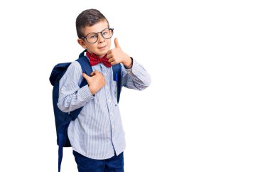 Sevimli sarışın çocuk inek papyonu ve sırt çantası takıyor mutlu ve pozitif gülümsüyor, başparmağını kaldırıyor ve işaret veriyor. 