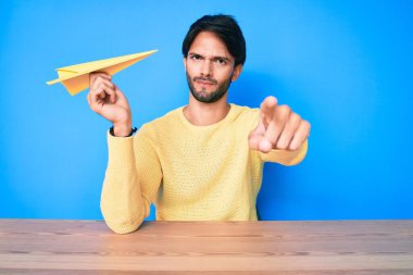 Elinde kağıt uçakla kamerayı gösteren yakışıklı İspanyol bir adam ve sen, kendine güvenen ciddi görünüyorsun. 