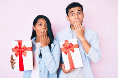 Güzel Latin genç çift yıldönümü kutlaması için hediye tutuyorlar ağızlarını ağızla kapatıyorlar, şok geçiriyorlar ve hata yapmaktan korkuyorlar. şaşırmış ifade 