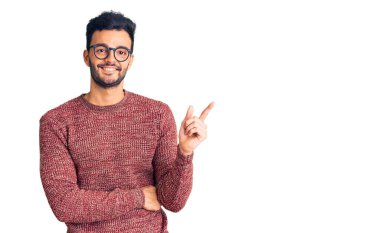 Kışlık süveter giyen ve yüzünde kocaman bir gülümseme olan genç, yakışıklı İspanyol adam kameraya el ve parmak ile bakıyor.. 