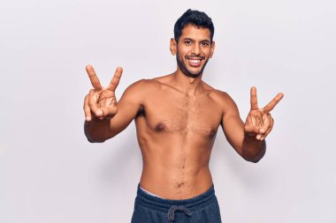 Genç Latin adam üstsüz bir şekilde kameraya bakıp zafer işareti yapıyor. İki numara.. 