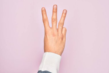 İzole edilmiş pembe arka planda parmaklarını gösteren beyaz bir gencin eli üç parmağı gösteriyor.