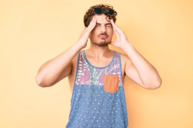 Kıvırcık saçlı, sıradan giyinen, kolsuz kolsuz tişörtlü, başı başı ağrıyan genç beyaz bir adam. migren ağrısı. 