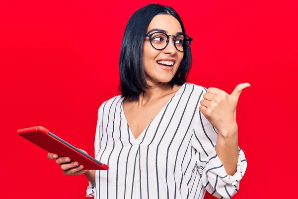 Young Beautiful Latin Woman Holding Touchpad Pointing Thumb Side Smiling — Stock Photo, Image