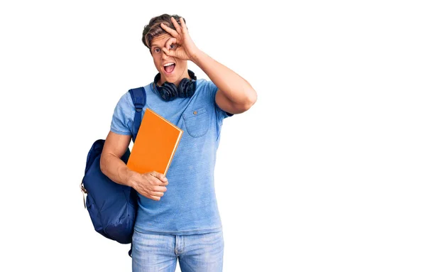 年轻英俊的男子背着学生背包 头戴耳机 高高兴兴地拿着书本 手拿着书 手拿着手拿着手拿着手拿着手拿着手拿着 手拿着手签 — 图库照片