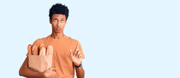 Joven Hombre Afroamericano Sosteniendo Bolsa Papel Con Pan Apuntando Hacia —  Fotos de Stock