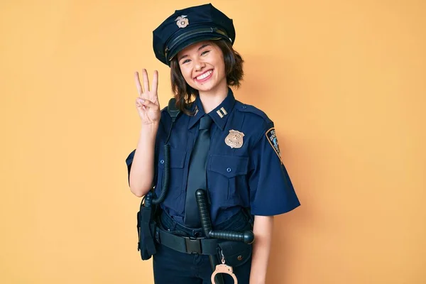 Young beautiful woman wearing police uniform showing and pointing up with fingers number three while smiling confident and happy.