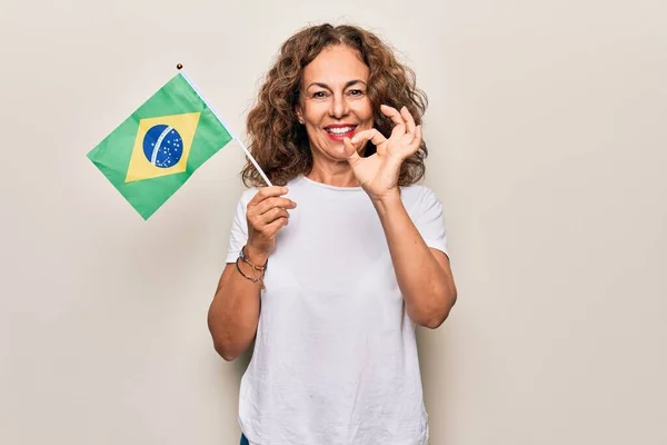 中年美丽的爱国女子举着巴西国旗 高高地挂在孤独的白色背景上 手握手签 微笑着友好的手势 是极好的象征 — 图库照片