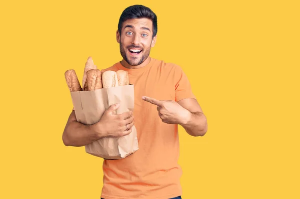 Young Hispanic Man Holding Paper Bag Bread Smiling Happy Pointing — Stock Photo, Image