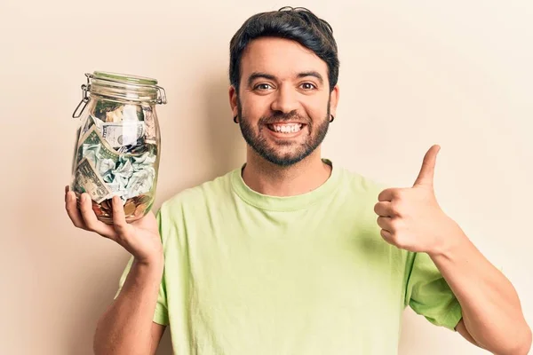 Joven Hombre Hispano Sosteniendo Frasco Con Ahorros Sonriendo Feliz Positivo —  Fotos de Stock