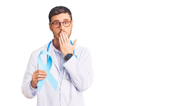 Przystojny Młodzieniec Mundurze Doktora Trzymający Niebieską Wstążkę Zakrywającą Usta Dłonią — Zdjęcie stockowe