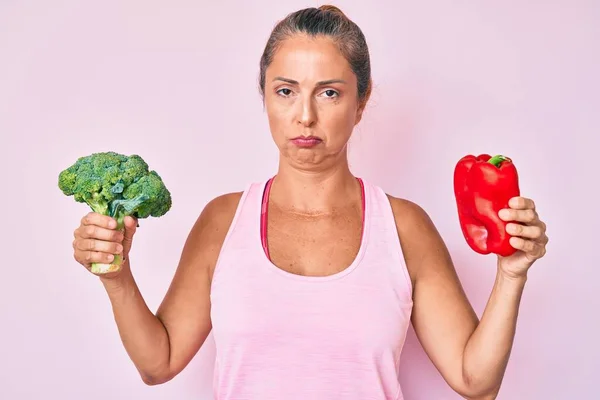 Mujer Hispana Mediana Edad Sosteniendo Brócoli Pimienta Roja Deprimida Preocupada —  Fotos de Stock