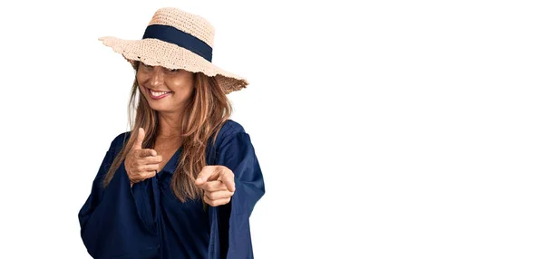 中世のヒスパニック系の女性が幸せと面白い顔を持つカメラに指を指して夏の帽子をかぶって 良いエネルギーと振動は — ストック写真