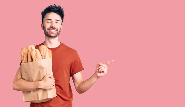 Young Hispanic Man Holding Paper Bag Bread Smiling Happy Pointing — Stock Photo, Image