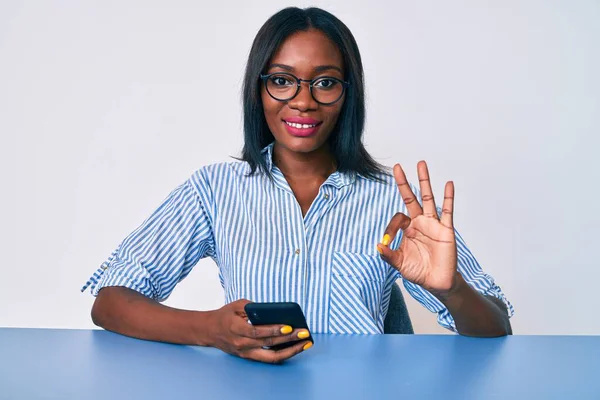 Młoda Afroamerykanka Pomocą Smartfona Siedzi Stole Robi Znak Palcami Uśmiechając — Zdjęcie stockowe