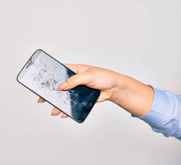 Hand of caucasian young woman holding broken smartphone showing craked screen over isolated white background